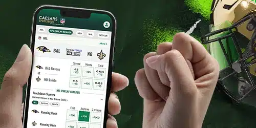 Close-up of a hand holding a smartphone displaying the Caesars Sportsbook app. The app shows NFL betting options, including team matchups, spread, moneyline, and total points, as well as a 'Touchdown Scorers' parlay builder. The background features a football helmet and green, abstract graphics